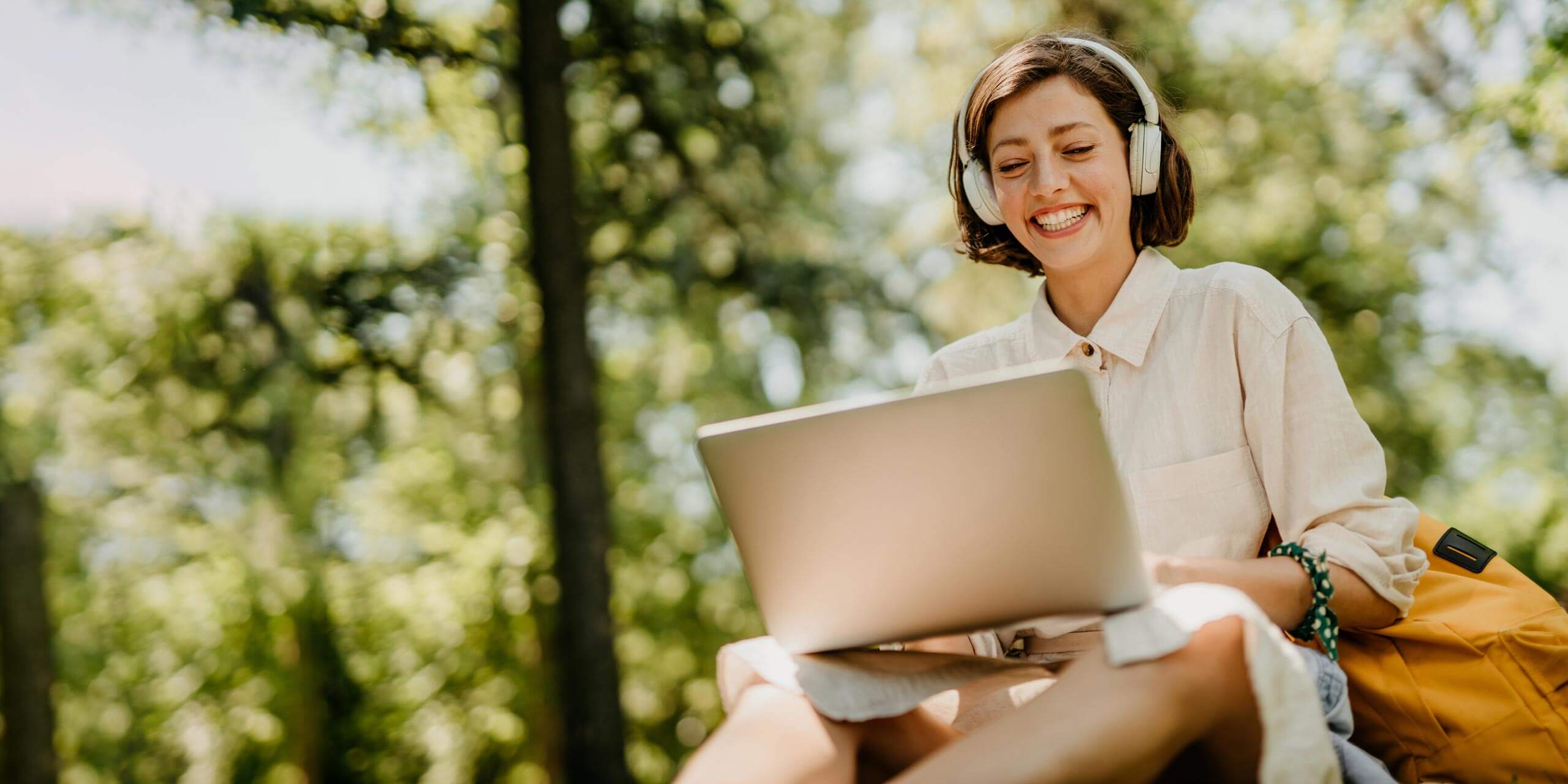Eine lächelnde Frau arbeitet an einem Laptop und genießt dabei die Ruhe eines sonnenbeschienenen Parks.